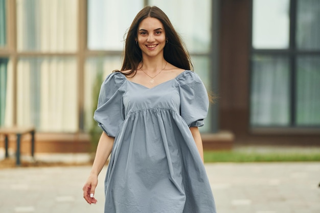 Hermosa mujer joven caminando en vestido en el exterior del edificio de la ciudad