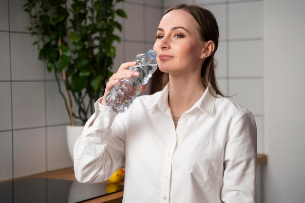 Hermosa mujer joven en una camisa blanca con cabello largo bebe agua de una botella de plástico sonríe y