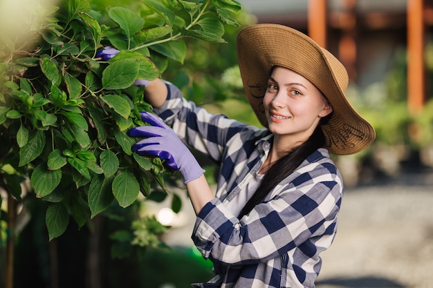 Hermosa mujer joven en camisa a cuadros y sombrero de paja jardinería exterior en verano.