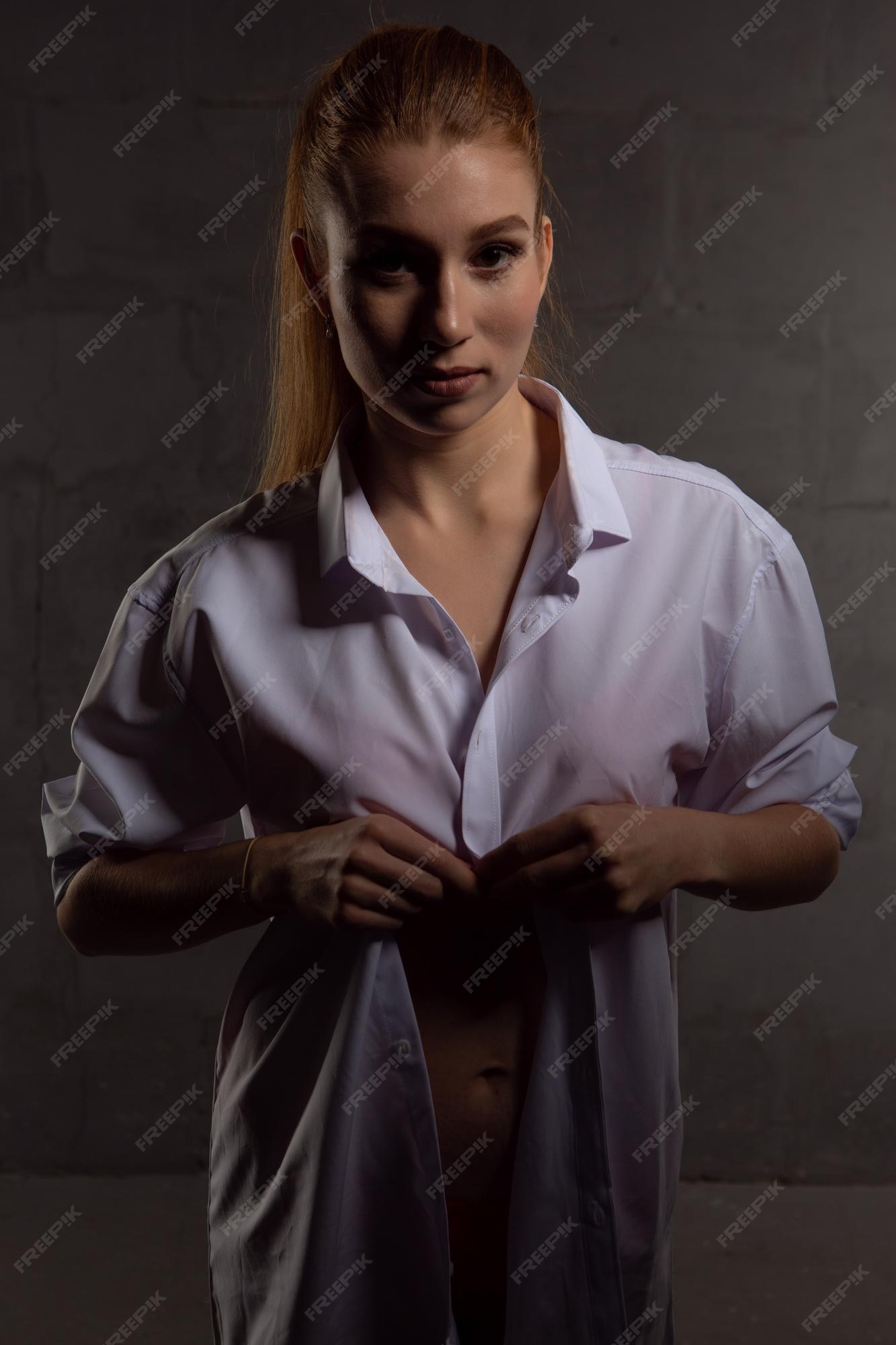 mujer joven en una camisa de hombre blanco posando en estudio sobre un fondo oscuro | Foto
