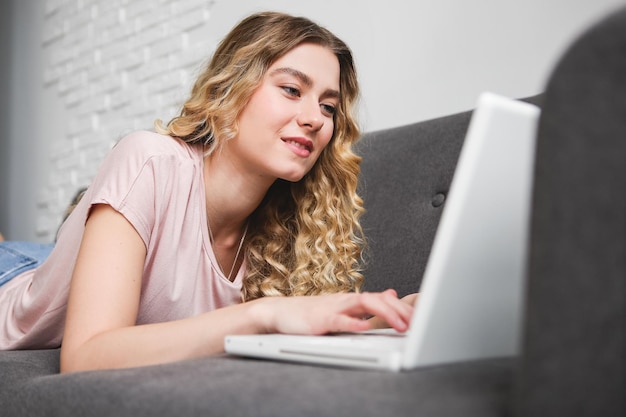 Hermosa mujer joven en camisa rosa trabajando en la computadora portátil Chica acostada en el sofá con el portátil Dis