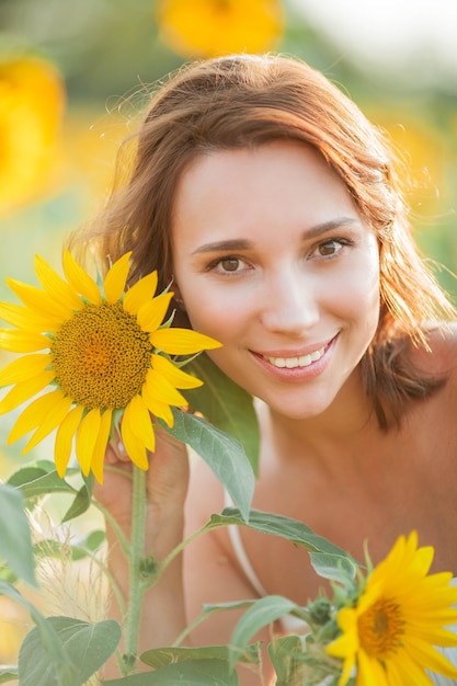 Hermosa mujer joven en el campo de girasol. Retrato de una mujer joven al sol. El verano.