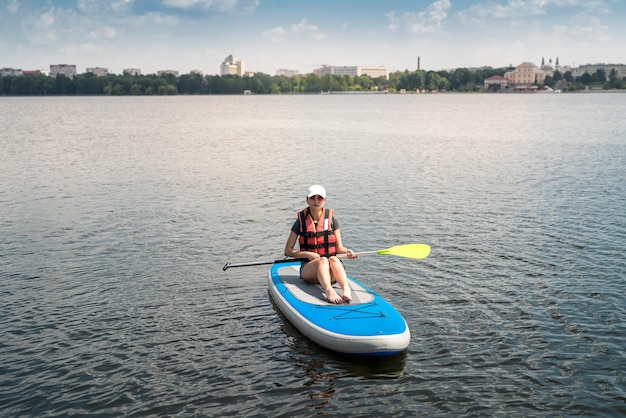 Hermosa mujer joven en un chaleco protector aprende a nadar en una tabla de sup en un lago de la ciudad estilo de vida activo horario de verano