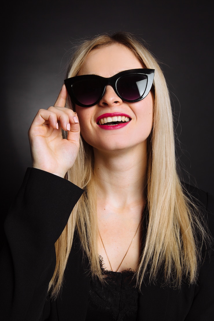 Hermosa mujer joven en chaqueta negra y gafas de sol sobre fondo negro. Bastante rubia chica