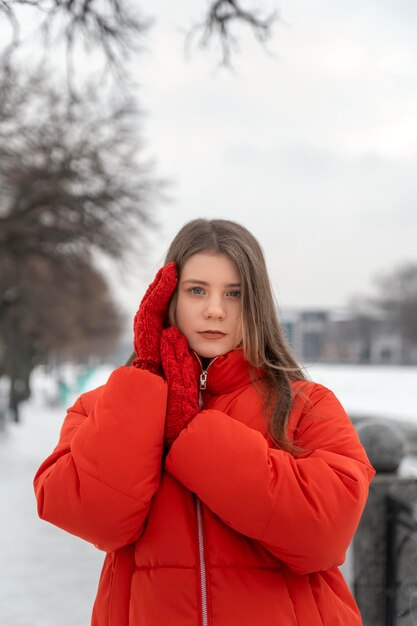 Hermosa mujer joven en chaqueta roja y mitones de punto mirada de tristeza en el parque de invierno