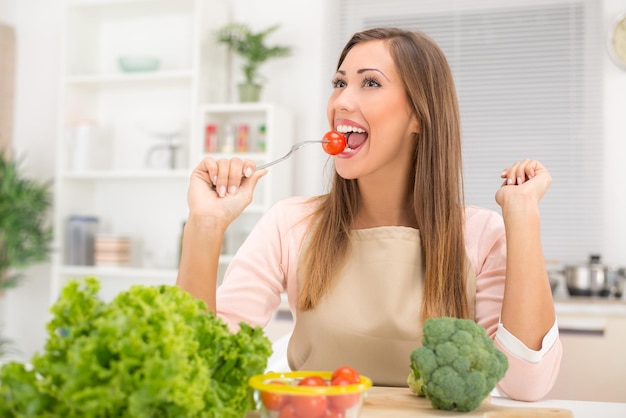 Hermosa mujer joven en la cocina comiendo tomate cherry rojo.