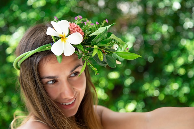 Foto hermosa mujer joven con una composición de flores naturales en la cabeza sobre un fondo borroso.