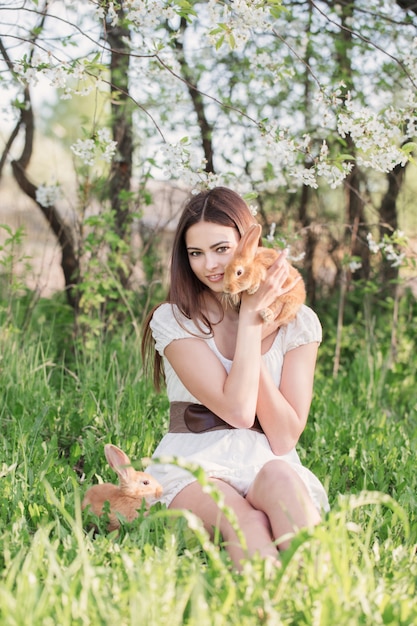 Hermosa mujer joven con conejos en el jardín