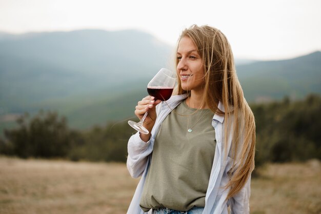 Hermosa mujer joven con una copa de vino tinto en las montañas