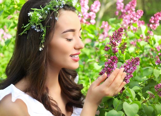 Hermosa mujer joven con corona de flores cerca de arbusto floreciente en un día soleado de primavera