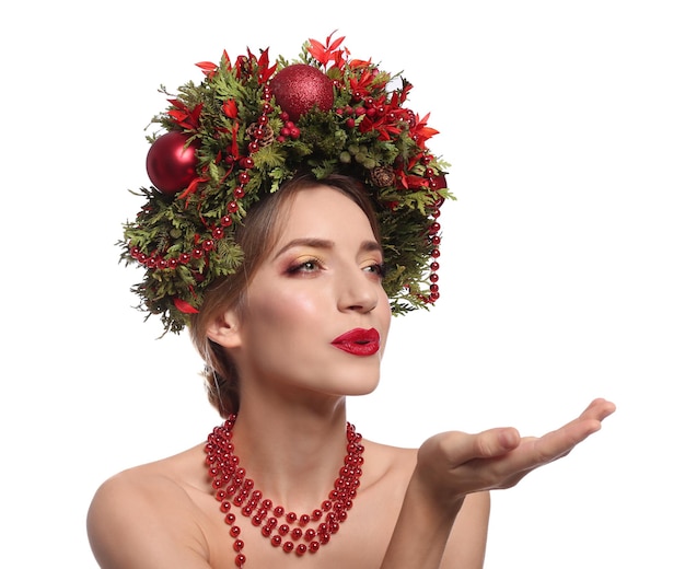 Foto hermosa mujer joven con corona de navidad soplando beso sobre fondo blanco.