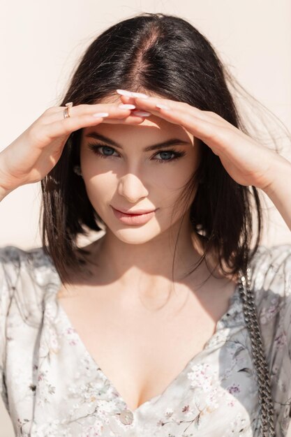 Hermosa mujer joven con un corte de pelo bob en un vestido vintage de moda cubre sus ojos azules en un día soleado y mira a la cámara