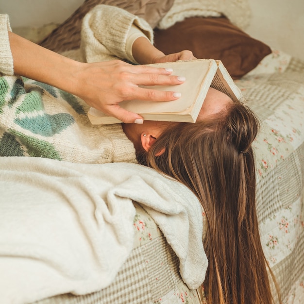 Hermosa mujer joven durmiendo en la cama con el libro que cubre su rostro porque leyendo el libro con la preparación del examen de la universidad, mujer soñolienta con cansado para que el ocio, el relax y el concepto de educación