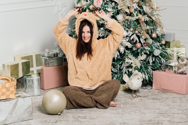 Hermosa mujer joven con un elegante vestido de pie junto al árbol de Navidad y regalos.