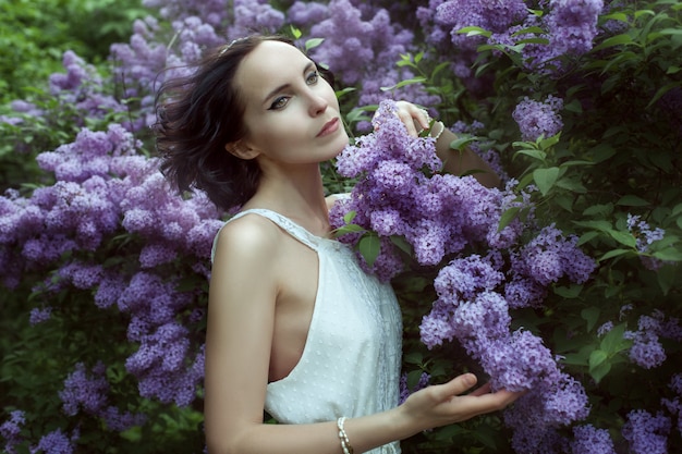 Hermosa mujer joven se encuentra entre los arbustos en flor lila en el jardín.