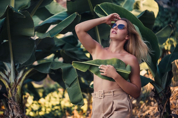 Hermosa mujer joven se encuentra en una hermosa pose cerca de un retrato de plátano en una plantación de plátanos