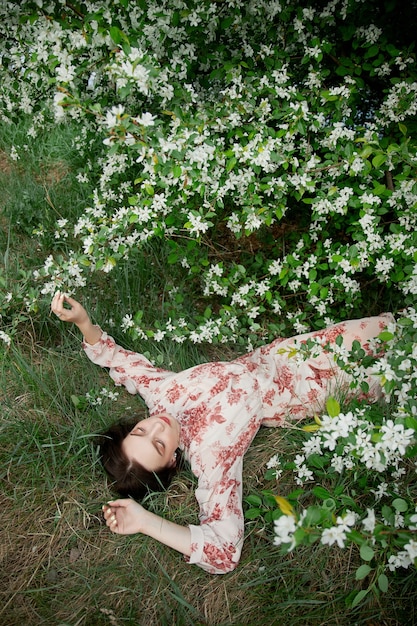 Hermosa mujer joven se encuentra en la hierba bajo el manzano en flor. Chica romántica descansa en la naturaleza. Primavera retrato de mujer