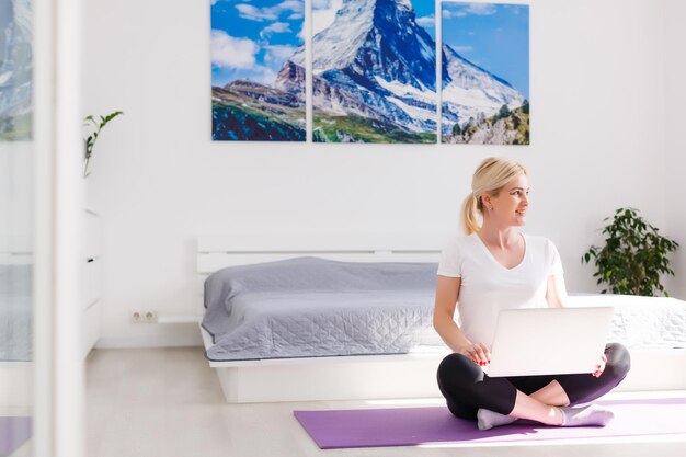 Hermosa mujer joven entrenando en línea en casa en la computadora portátil, espacio de copia. Retrato de cuerpo entero. Yoga, pilates, hacer ejercicio