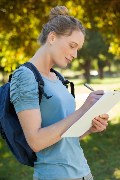 Hermosa mujer joven escribiendo en portapapeles en el parque