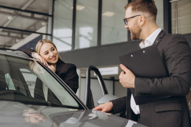 Una hermosa mujer joven está hablando con un guapo trabajador de un concesionario de automóviles mientras elige un coche
