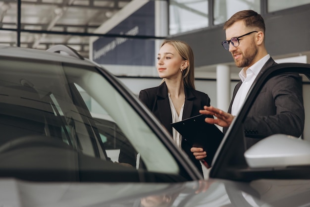 Una hermosa mujer joven está hablando con un guapo trabajador de un concesionario de automóviles mientras elige un coche
