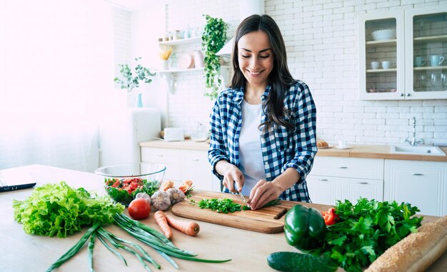 Hermosa mujer joven está preparando ensalada de verduras en la cocina. Comida sana. Ensalada Vegana. Dieta. Concepto de dieta. Estilo de vida saludable. Cocinar en casa. Prepara comida. Cortar los ingredientes en la mesa