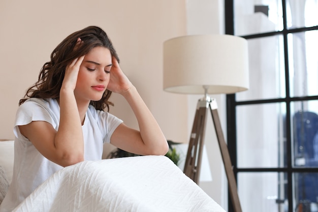 Hermosa mujer joven está sentada en la cama porque tiene un dolor de cabeza largo.