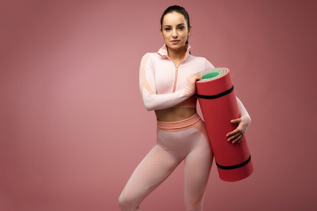 Foto hermosa mujer joven con estera de yoga posando en el estudio