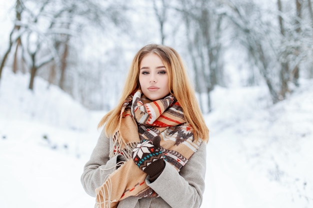 Hermosa mujer joven con estilo con una bufanda de lana vintage en un elegante abrigo con guantes calientes