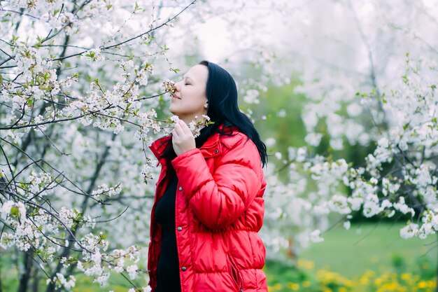 Hermosa mujer joven feliz camina en un florido jardín de primavera con cerezos en flor