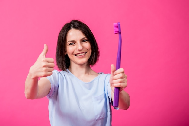 Hermosa mujer joven feliz con cepillo de dientes grande sobre fondo rosa en blanco