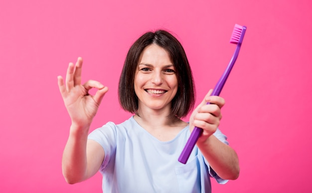 Hermosa mujer joven feliz con cepillo de dientes grande sobre fondo rosa en blanco