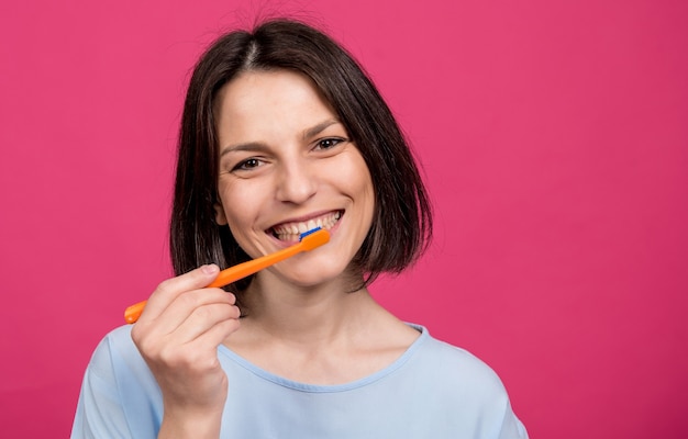 Hermosa mujer joven feliz con cepillo de dientes sobre fondo rosa en blanco