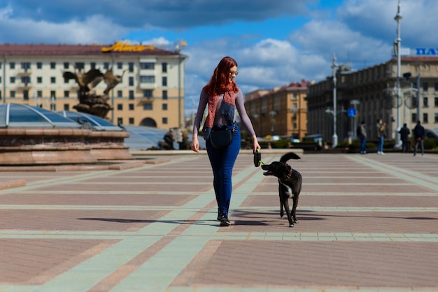 Hermosa mujer joven feliz con lindo perro negro divertirse en la calle. Concepto de amistad entre animales y personas.