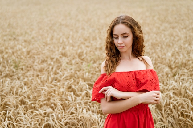 Hermosa mujer joven feliz con el pelo rizado en un vestido rojo posando en un campo de trigo