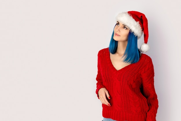 Hermosa mujer joven feliz con sombrero de santa sobre fondo gris. Concepto de venta de compras navideñas