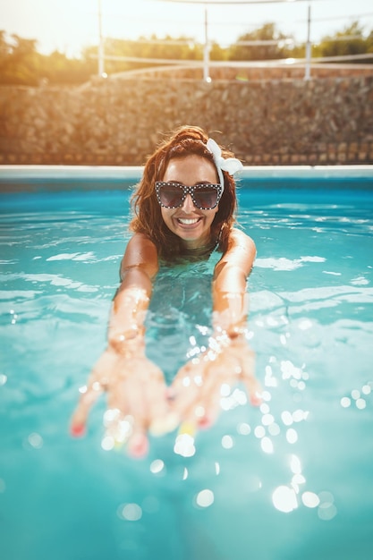 Hermosa mujer joven feliz sonriente está disfrutando en la piscina. Ella está lista para nadar en agua azul clara.