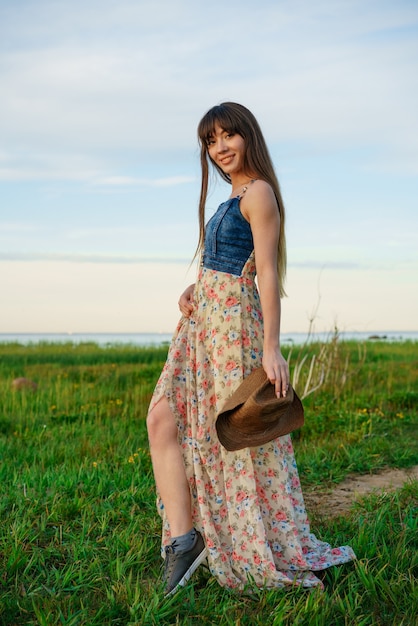 Hermosa mujer joven feliz suelta en un vestido en la naturaleza y con sombrero