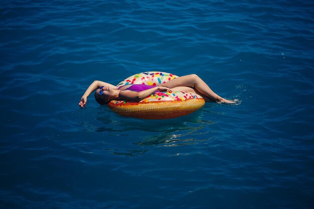 Hermosa mujer joven feliz en traje de baño con un anillo inflable relajante en el mar azul Día soleado turismo de vacaciones junto al mar