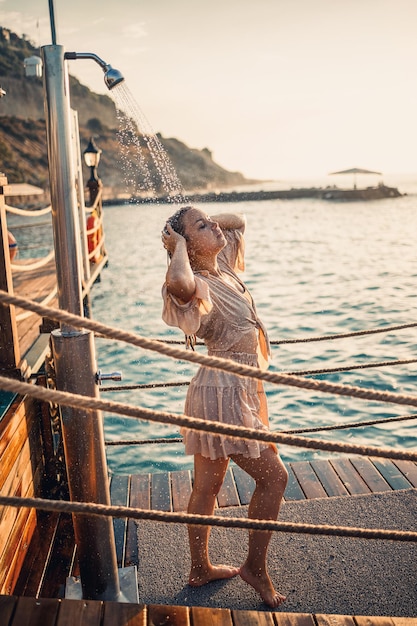 Hermosa mujer joven con una figura perfecta en la ducha bajo los rayos de la puesta de sol junto al mar La chica con un bronceado dorado de vacaciones Enfoque selectivo