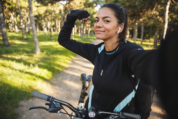 Hermosa mujer joven fitness con ropa deportiva en bicicleta al aire libre, tomando un selfie