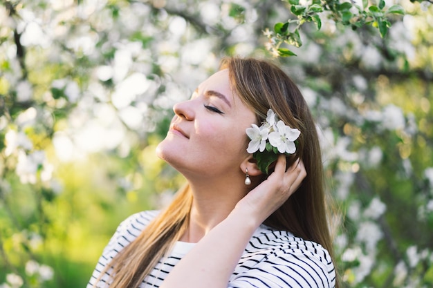 Hermosa mujer joven con flores de primavera disfrutando de la naturaleza y riendo en el jardín de primavera