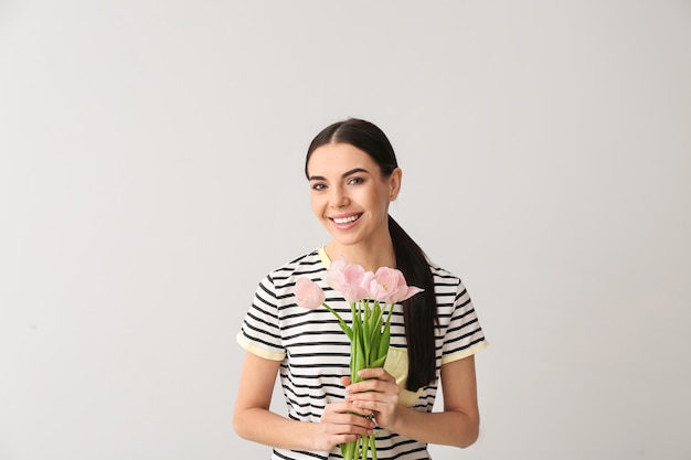 Hermosa mujer joven con flores en superficie gris