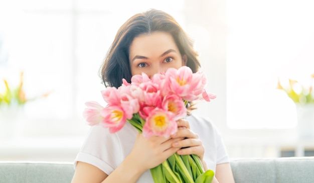 Hermosa mujer joven con flores tulipanes en las manos sentada en el sofá en casa