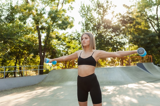 Hermosa mujer joven en forma haciendo ejercicio matutino con pesas al aire libre.