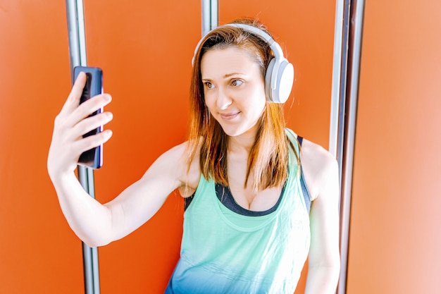 Hermosa mujer joven en forma tomando un selfie en el vestuario del gimnasio. concepto de deporte y tecnología