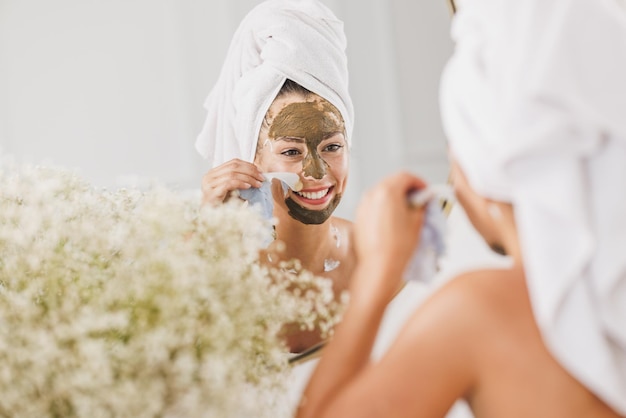 Hermosa mujer joven frente al espejo quitando la máscara facial en el salón de belleza.