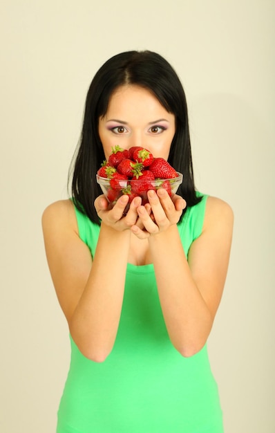 Foto hermosa mujer joven con fresas sobre fondo gris