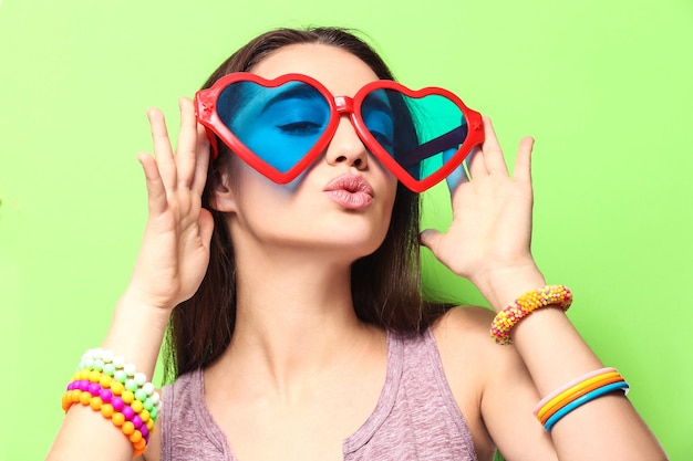 Hermosa mujer joven con gafas en forma de corazón sobre fondo de color