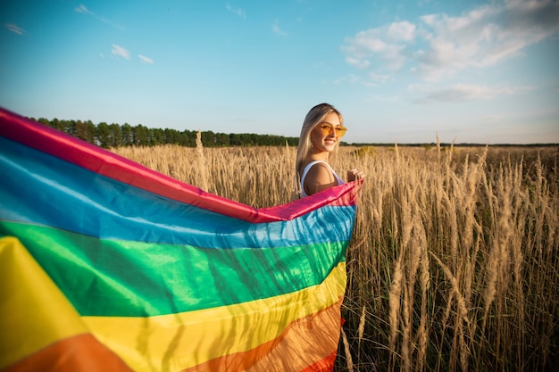 Hermosa mujer joven en gafas de sol con bandera lgbt en un campo